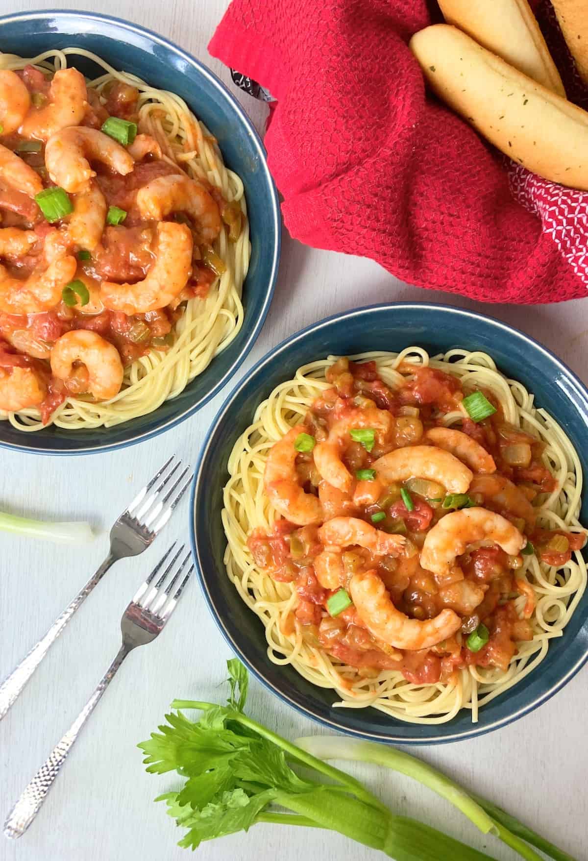 Two blue bowls with creole shrimp pasta garnished with green onions.