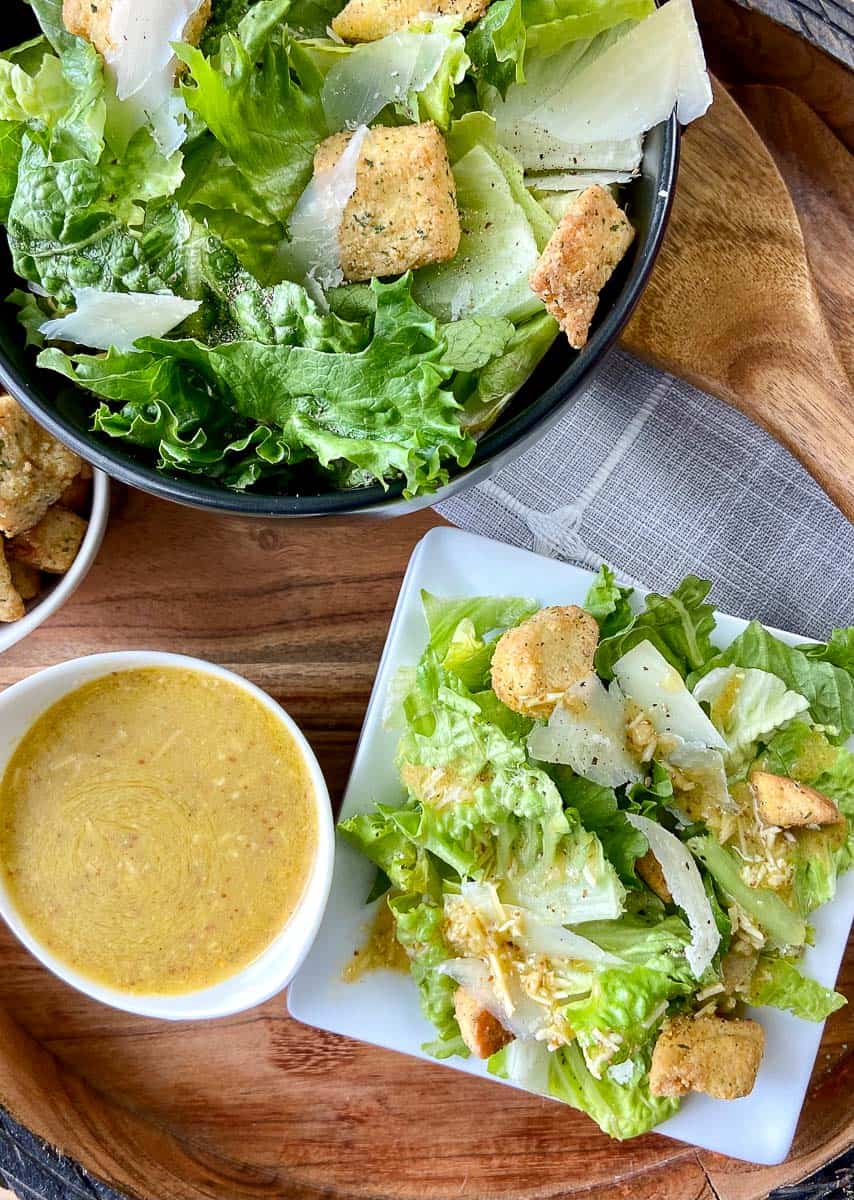 Caesar salad dressing in a bowl next to salad.