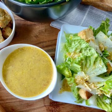 Caesar dressing in small bowl next to Caesar salad