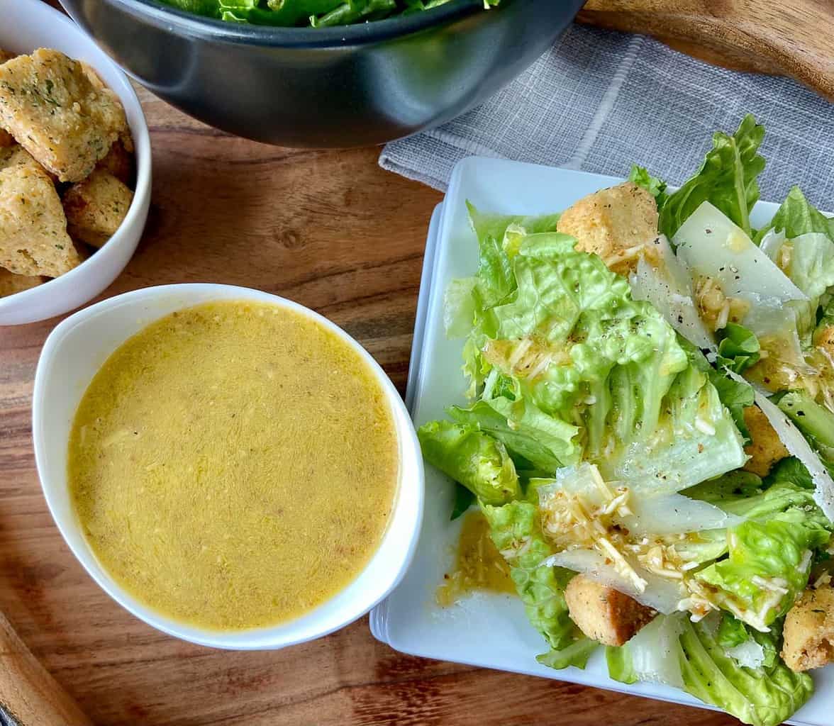 Caesar dressing in small bowl next to Caesar salad