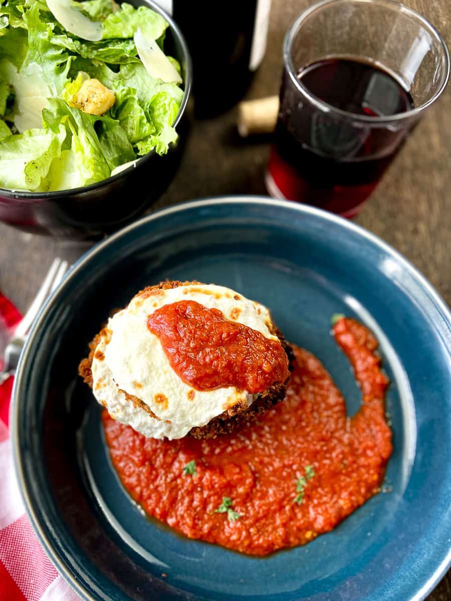 Crispy fried eggplant parmesan in blue dish drizzled with pasta sauce