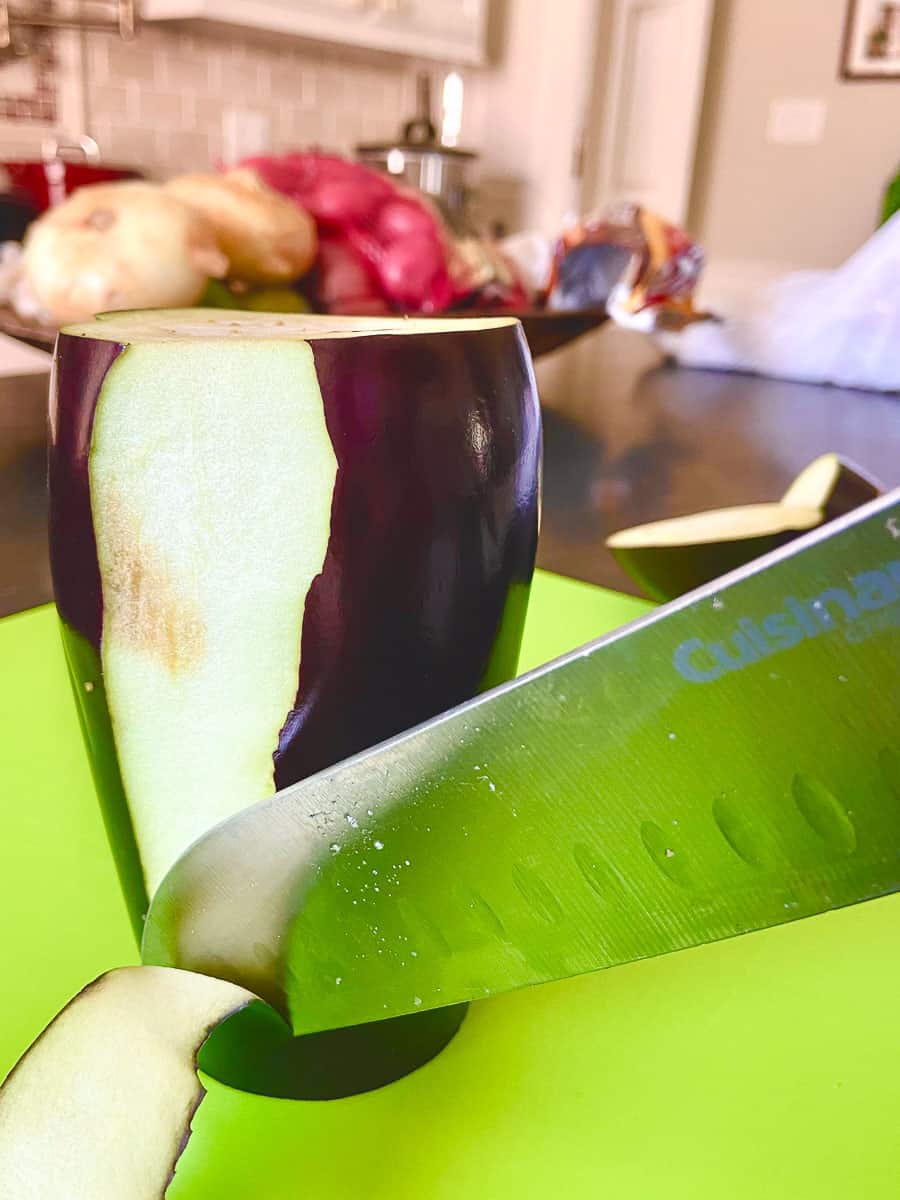 Knife slicing off purple skin of eggplant