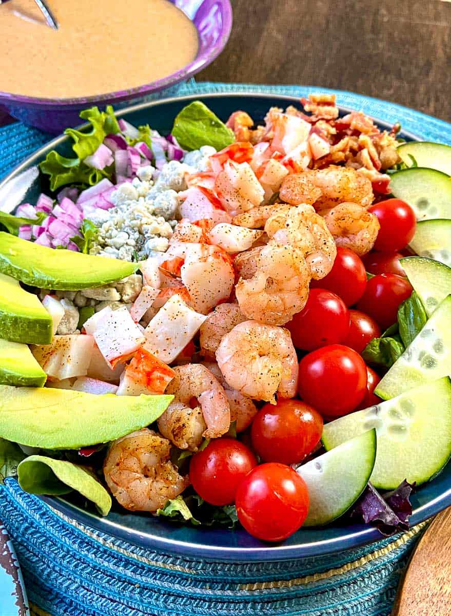 Seafood Cobb Salad in a shallow blue bowl with dressing on the side