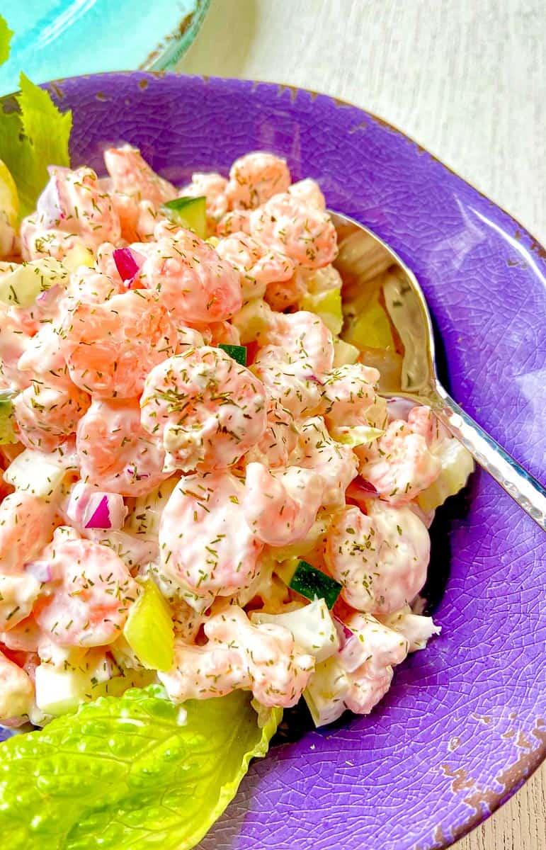 Shrimp salad in purple bowl with serving spoon.