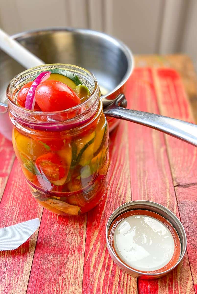 Jar of marinated cucumber salad on wooden table.