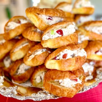 Chicken salad sandwiches on mini croissants stacked on silver platter.