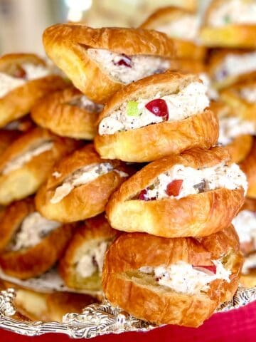 Chicken salad sandwiches on mini croissants stacked on silver platter.