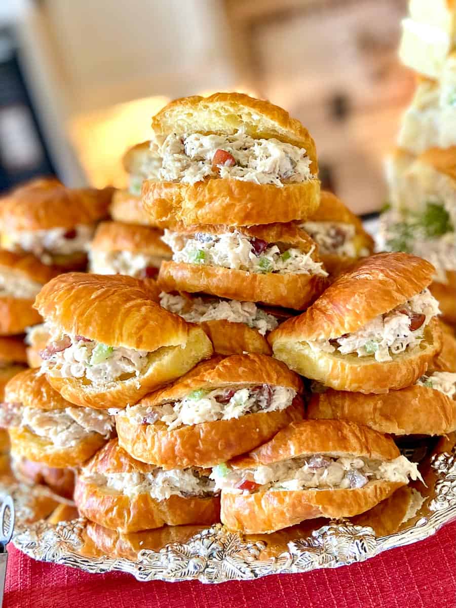 Chicken salad sandwiches on mini croissants stacked on silver platter.