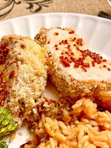 Sliced pork tenderloin with mustard, brown rice and broccoli on white plate.