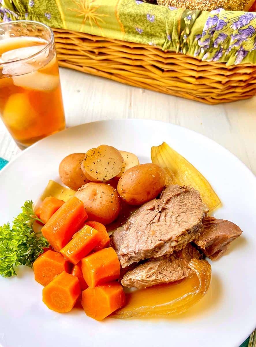 Pot roast with carrots, potatoes and onions on white plate.