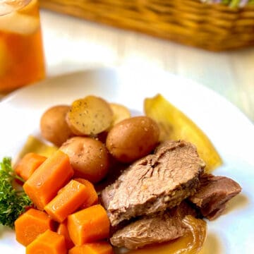 Sliced pot roast with onions, carrots and potatoes on white plate.