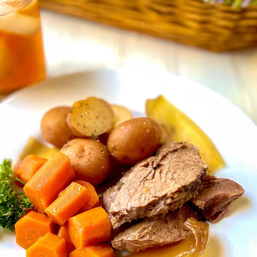 Sliced roast with onions, carrots and potatoes on white plate.