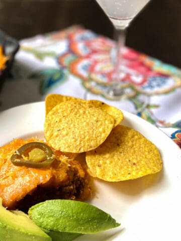 Tamale Pie on plate with sliced avocado and tortilla chips.