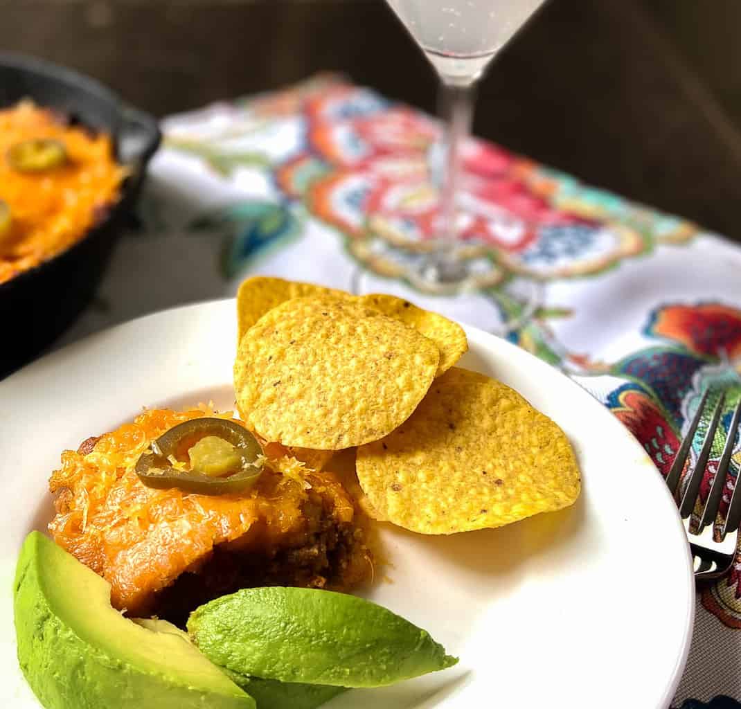 Tamale Pie on plate with sliced avocado and tortilla chips.