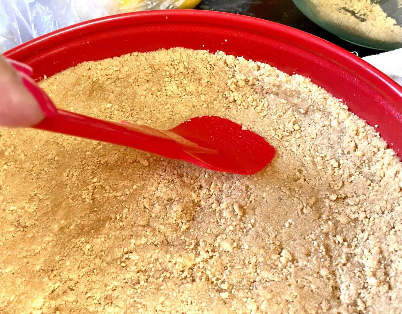 Graham cracker crust being pressed into pan with spatula.