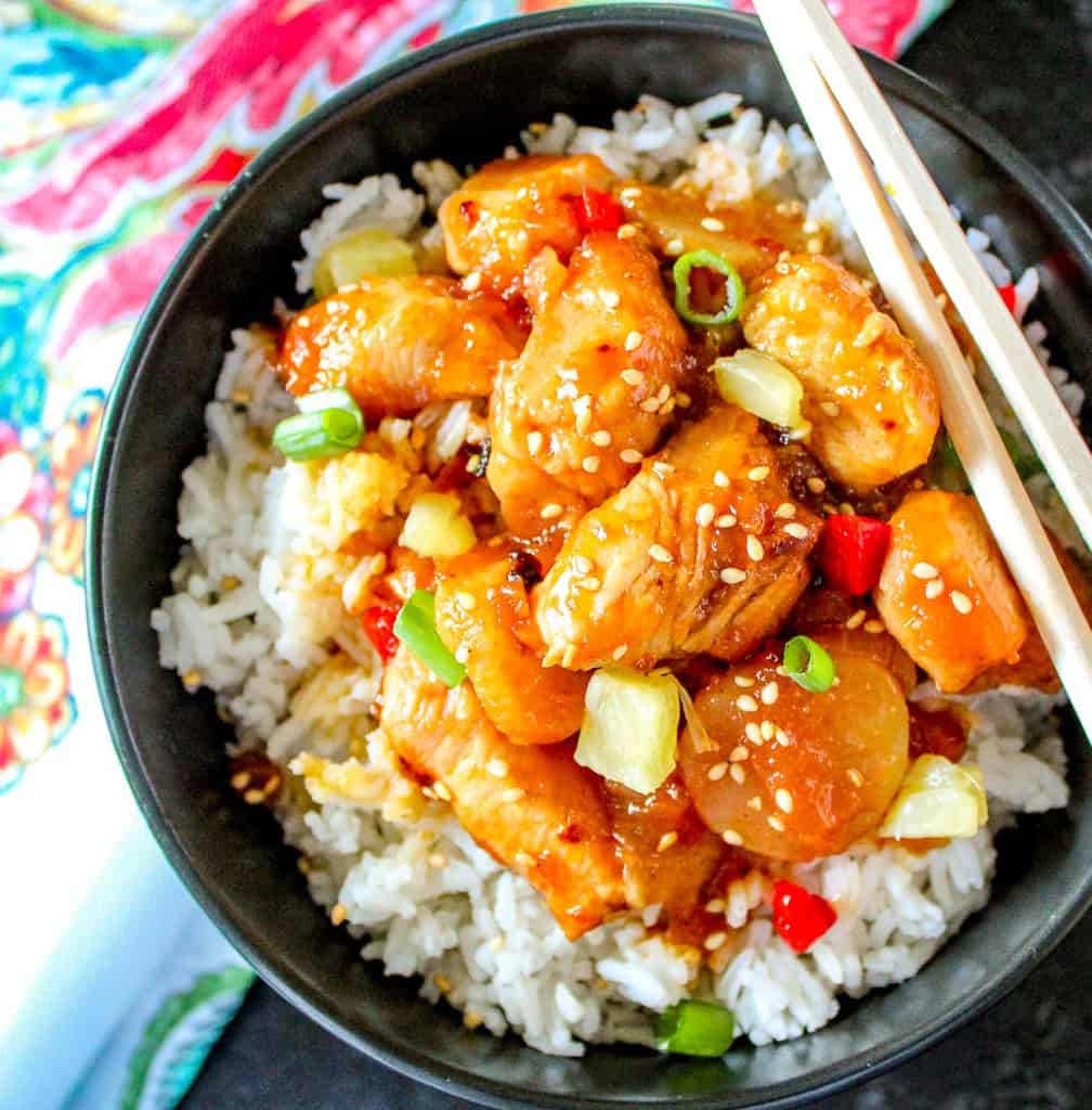 Sweet and sour shrimp on rice in black bowl.