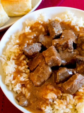 Beef tips, rice and gravy in white bowl.