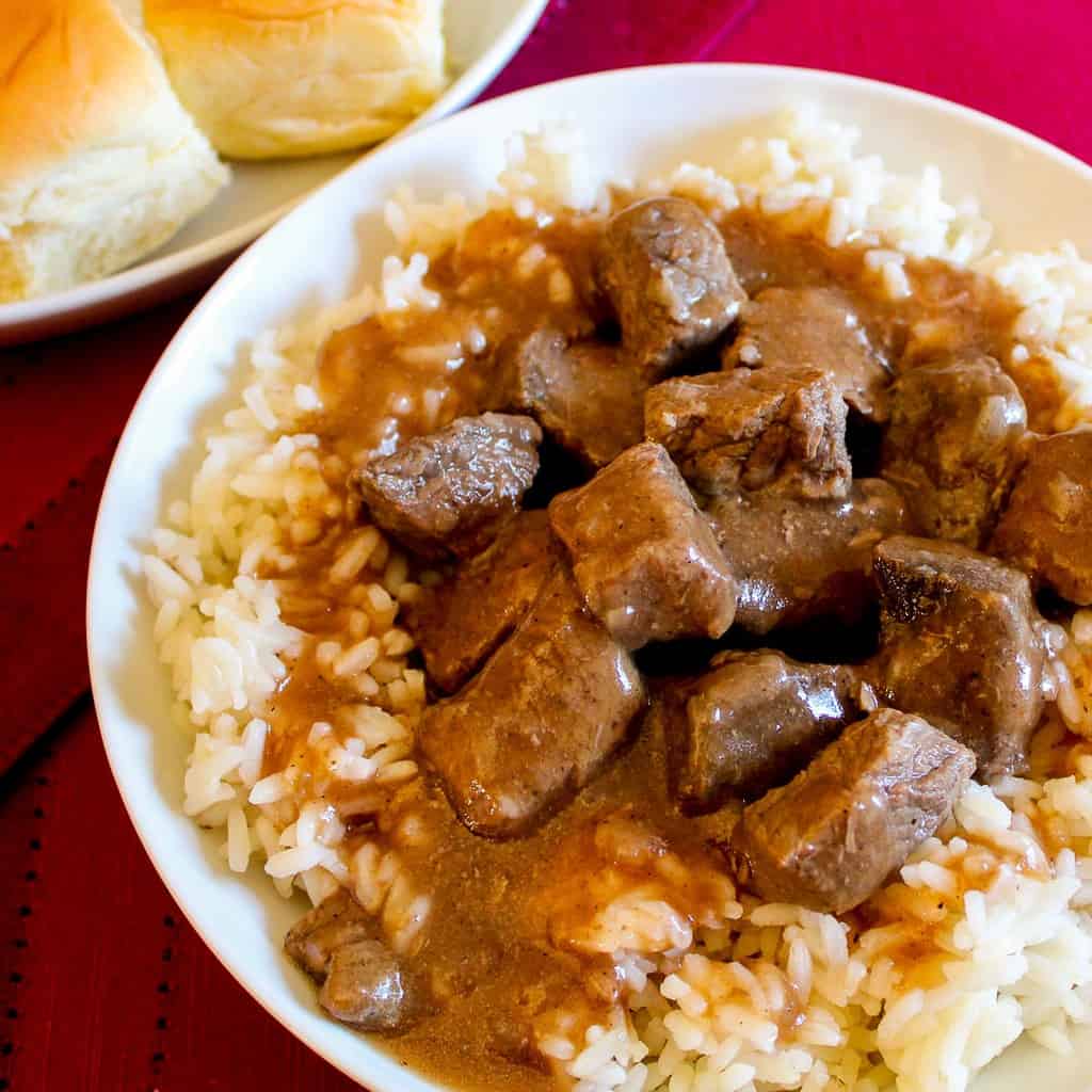 Beef tips, rice and gravy in white bowl.