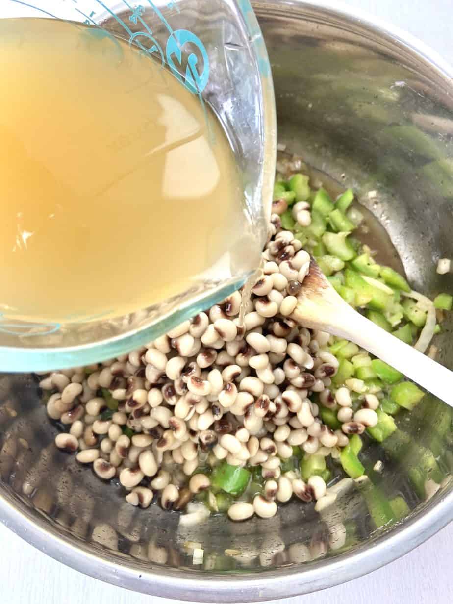 Homemade chicken broth being added to peas in stockpot.