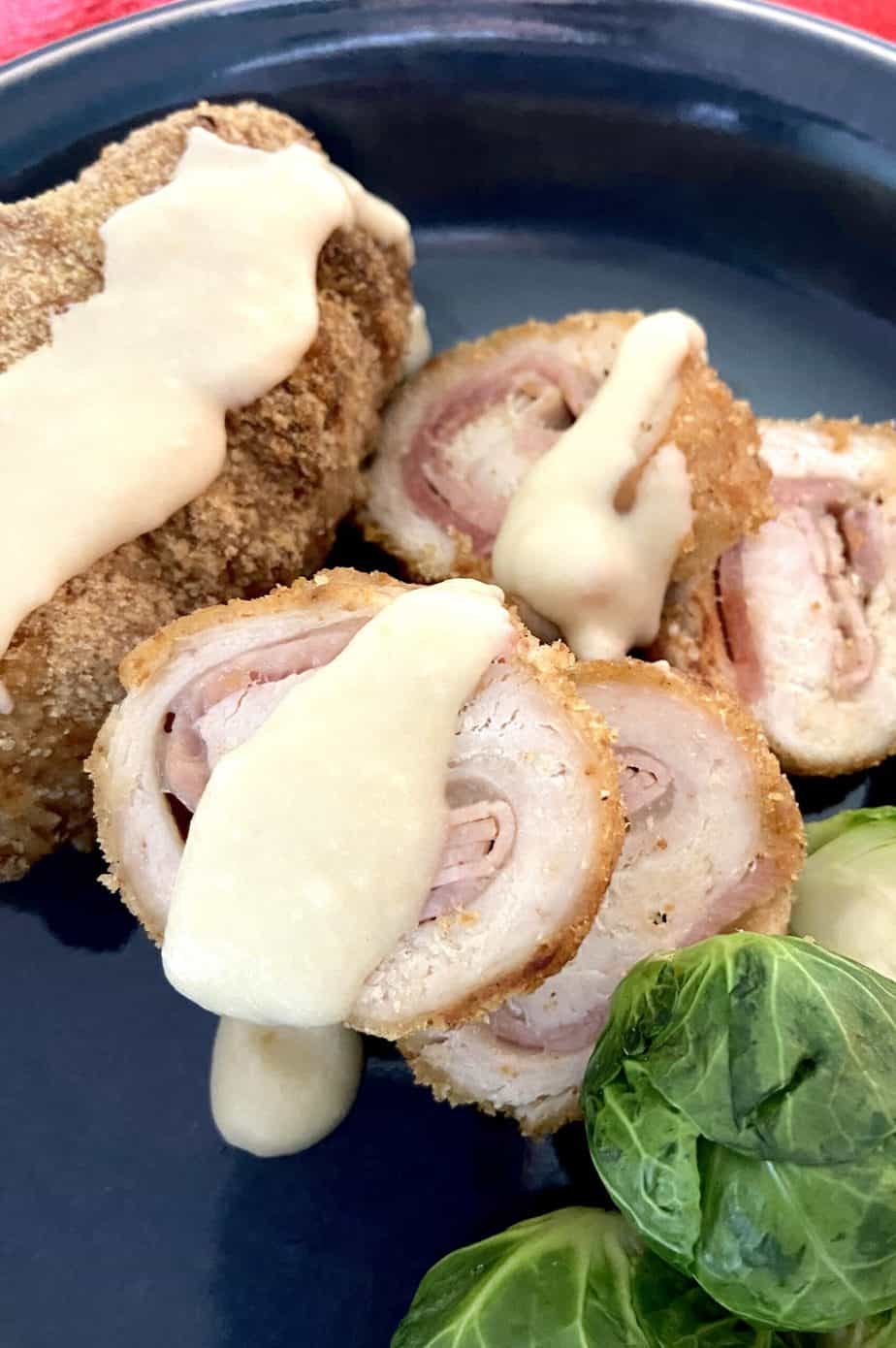 Sliced cordon bleu with sauce on blue plate.