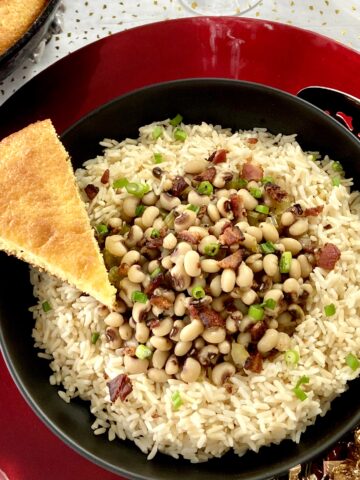 Hoppin john in black bowl with slice of cornbread.