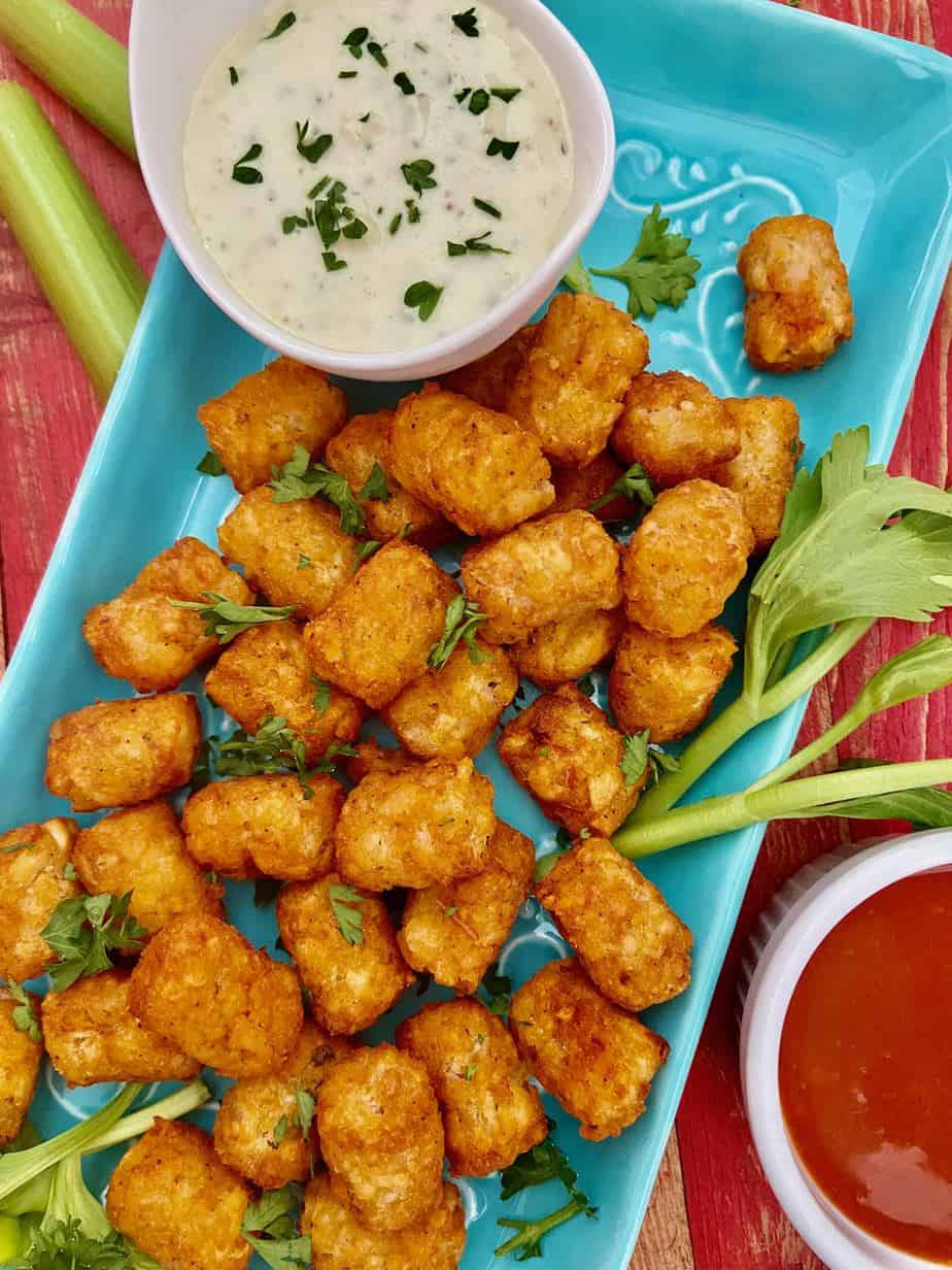 Buffalo Tater Tots with a side of Blue Cheese Aioli on turquoise plate.