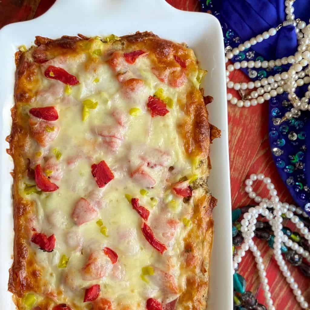 Mardi Gras Muffaletta Layer Dip in baking dish with beads on the side.