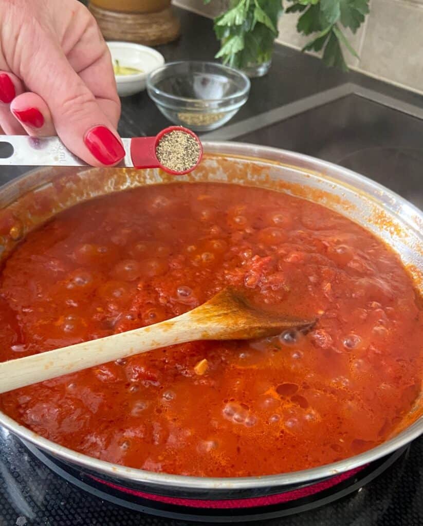Black pepper being added to tomato sauce in pan.