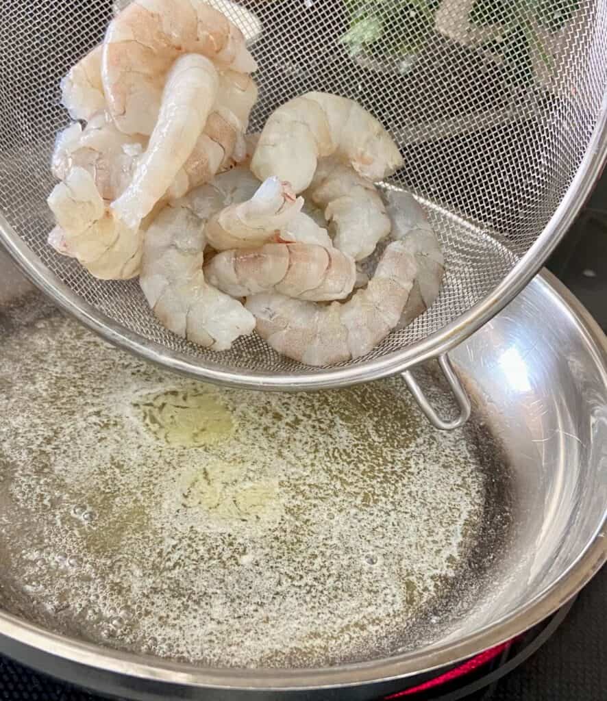 Shrimp being added to saucepan with melted butter.