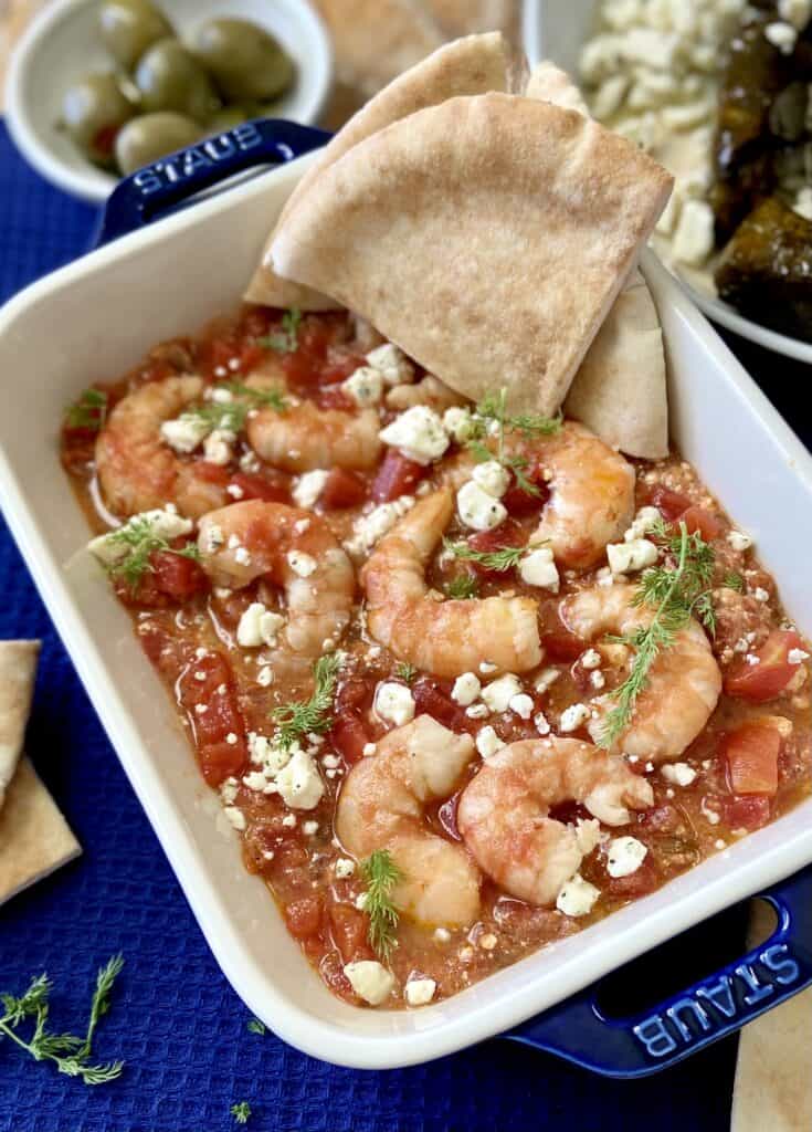 Baked Greek Shrimp in a white baking dish with pita bread on the side.