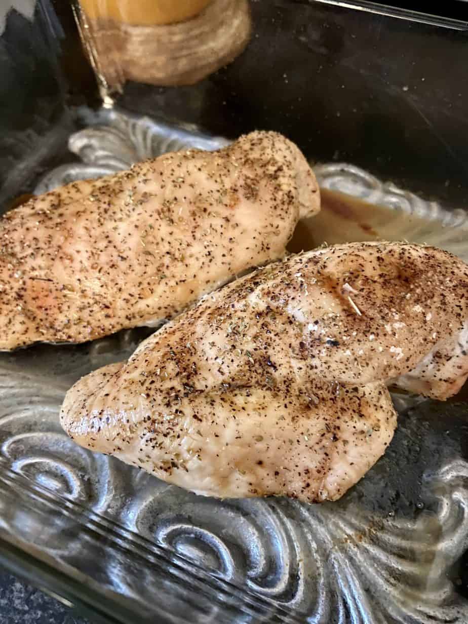 Two golden brown baked chicken breasts in glass baking dish.