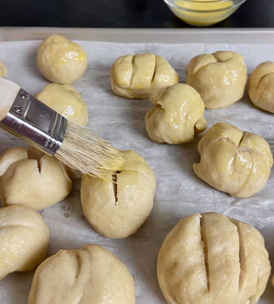 Pretzel dough being brushed with egg wash with pastry brush.