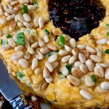 Close up of cheese ring garnished with pinenuts and green onion with orange jam in the center.