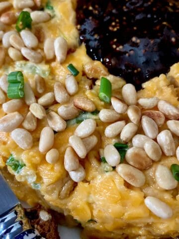 Close up of cheese ring garnished with pinenuts and green onion with orange jam in the center.