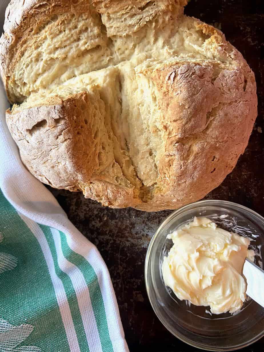 Round loaf of baked bread scored into quarters with butter on the side.