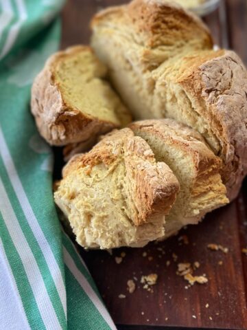 Round loaf of bread cut into quarters on dark brown cutting board.