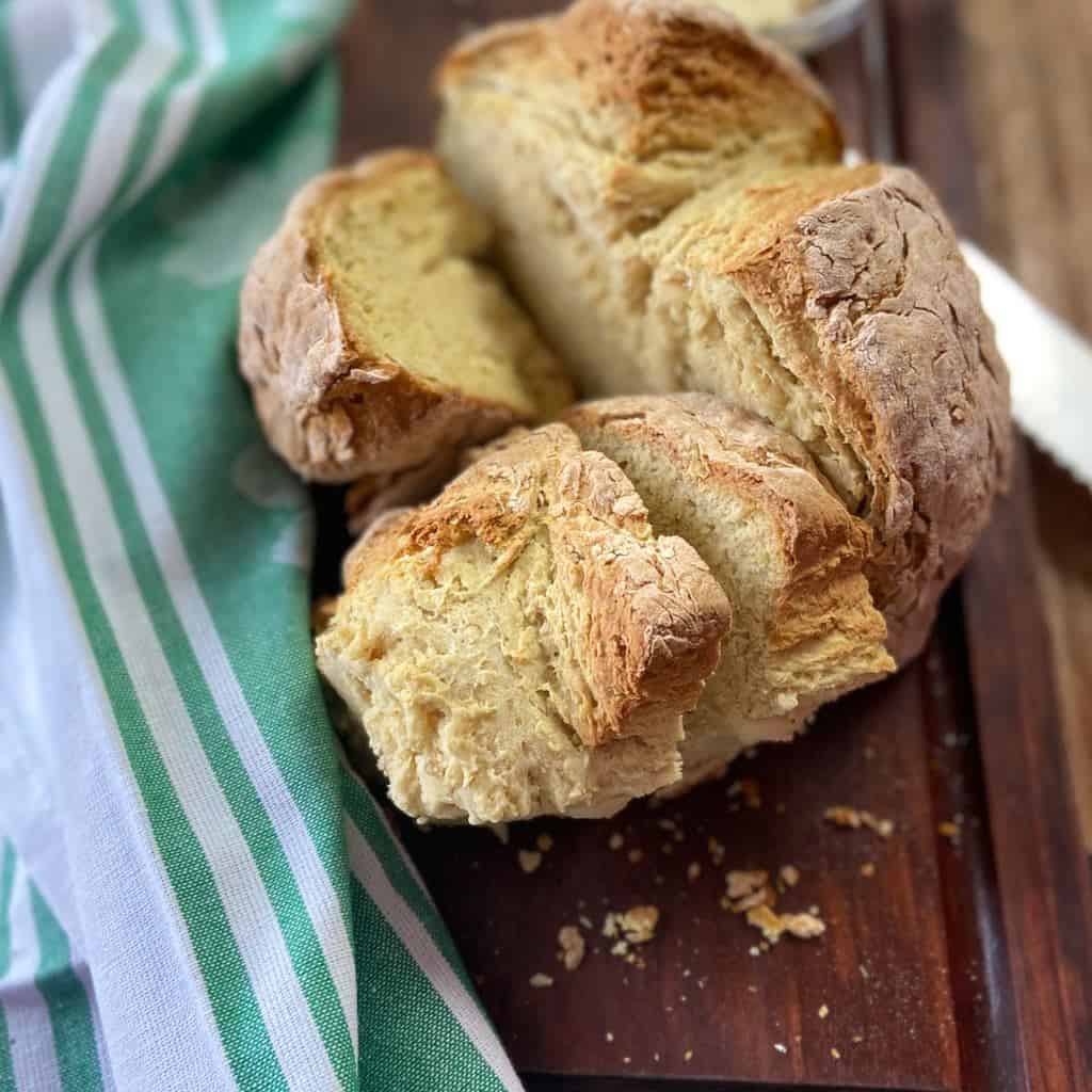 Round loaf of bread cut into quarters on dark brown cutting board.