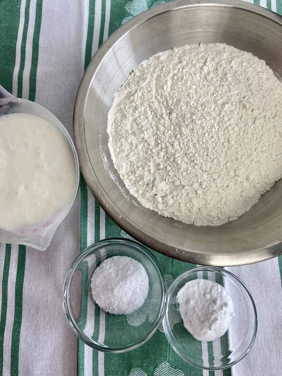 Flour, baking soda, salt and buttermilk in bowls on countertop.