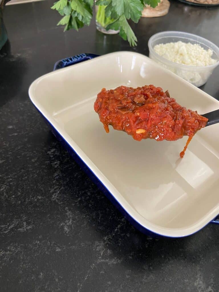 Tomato sauce being ladeled into baking dish.