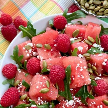Watermelon salad garnished with arugula and goat cheese in white bowl.