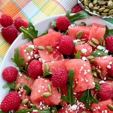 Watermelon salad garnished with arugula and goat cheese in white bowl.