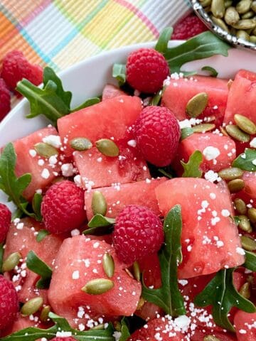 Watermelon salad garnished with arugula and goat cheese in white bowl.