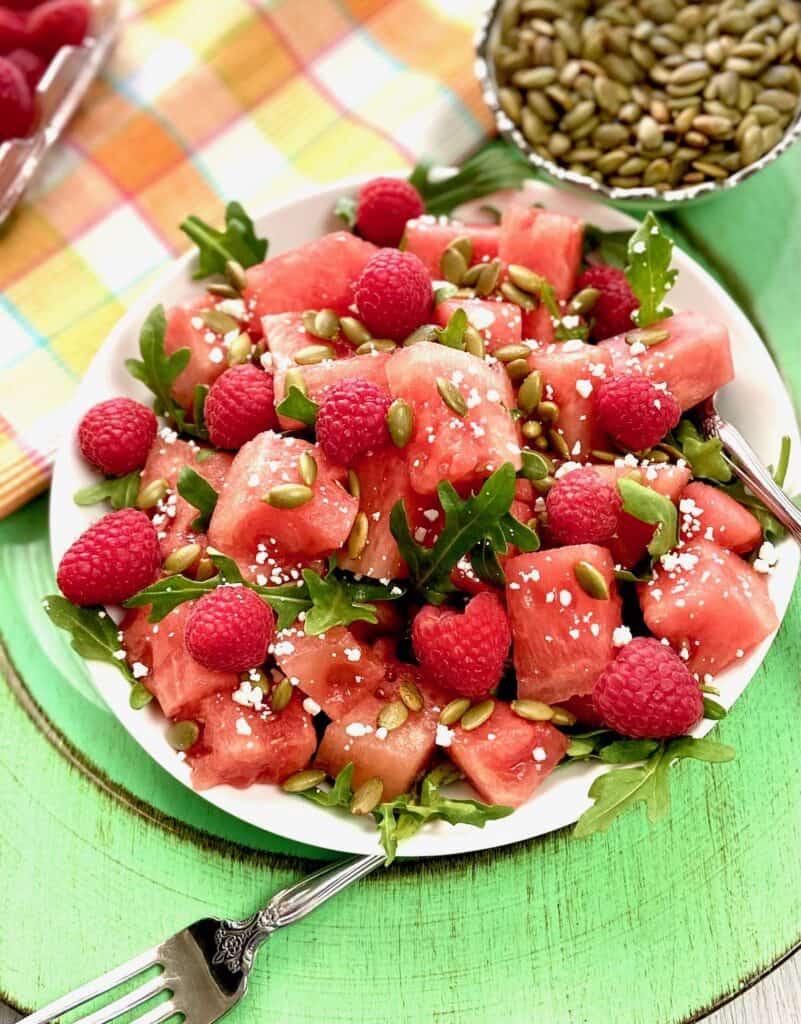 Watermelon salad garnished with arugula and goat cheese in white bowl.