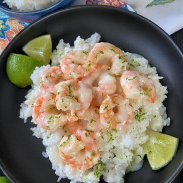 Shrimp in creamy coconut sauce over rice in black bowl.