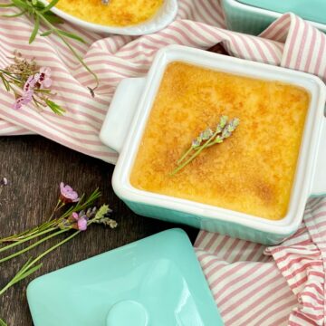 Square turquoise ramekin of creme brulee garnished with sprigs of lavender.