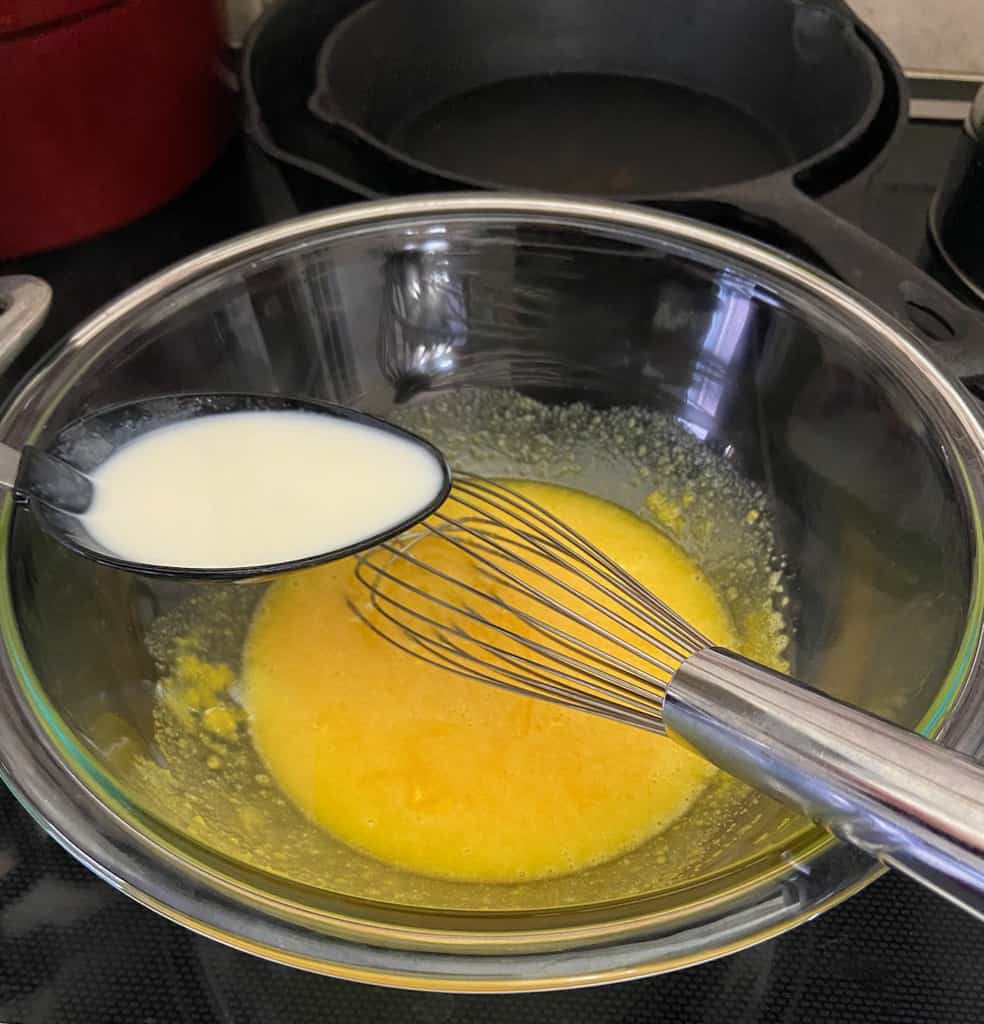 Spoonful of hot custard being added to egg yolks.