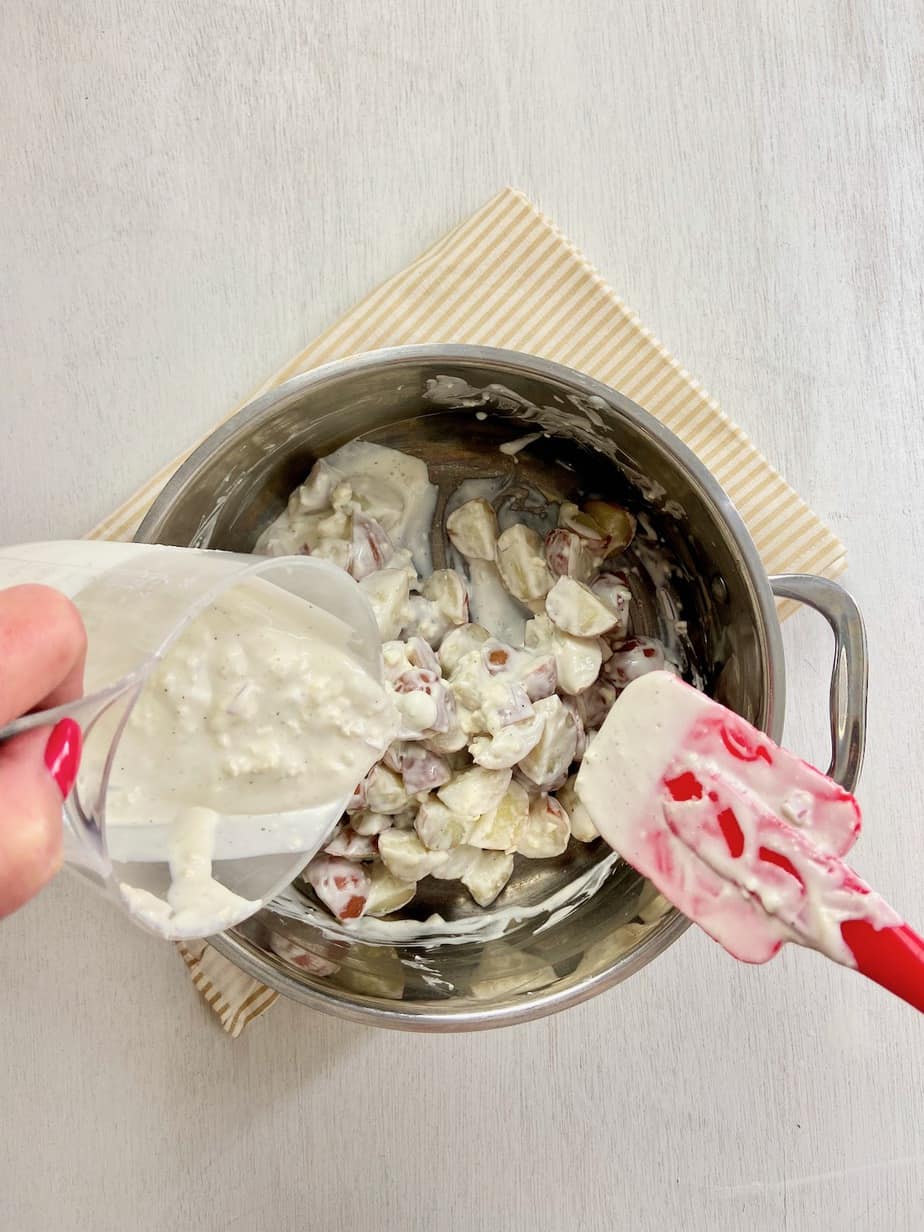 Potatoes in stockpot with blue cheese dressing being folded in with spatula.