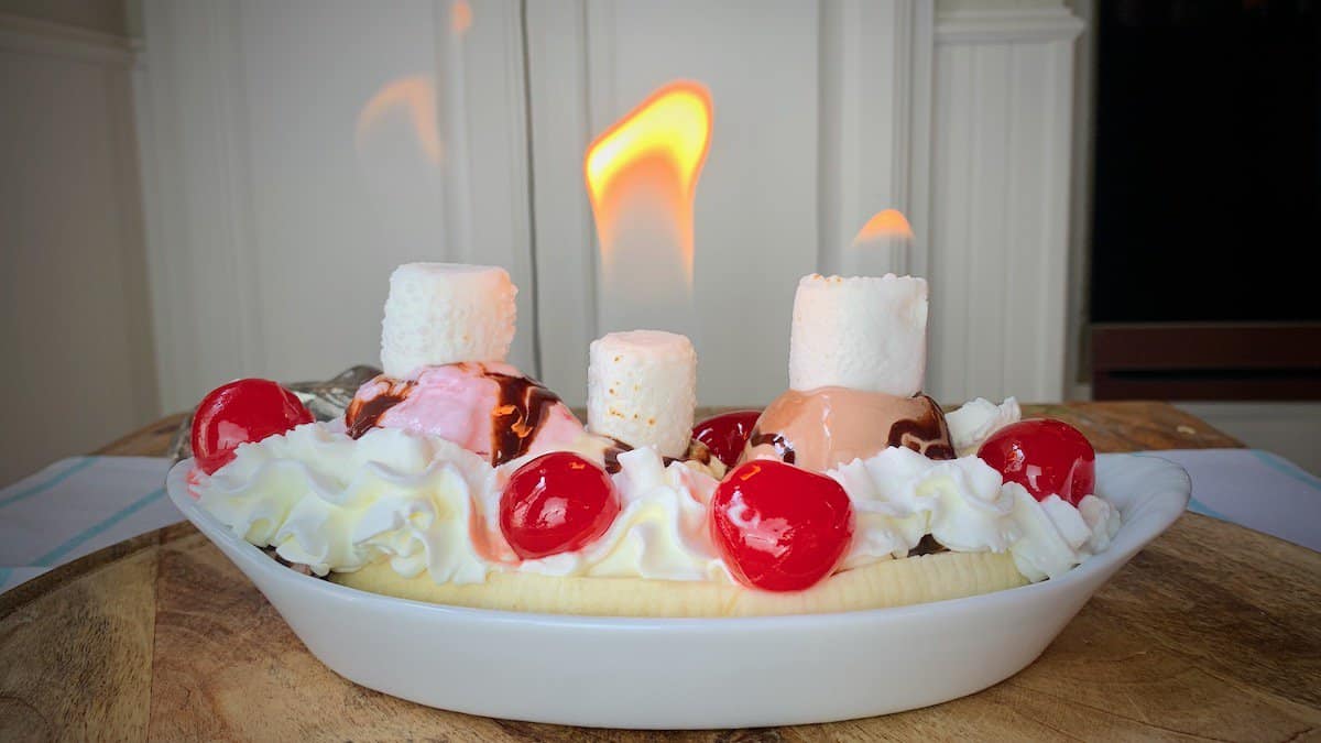 Flaming banana split in white dish.