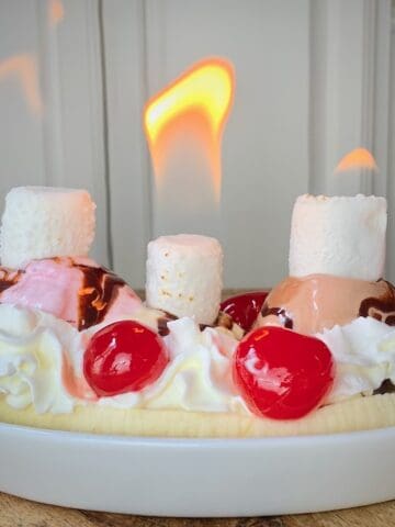 Flaming banana split in white dish.