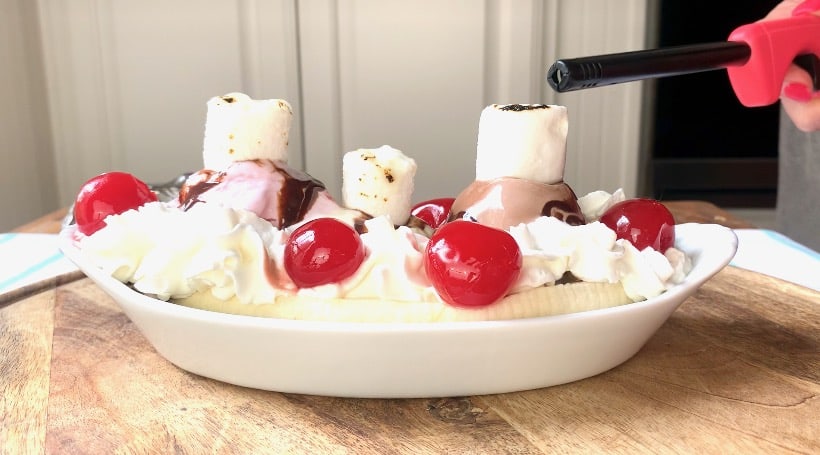 Banana split with cherries in white bowl.